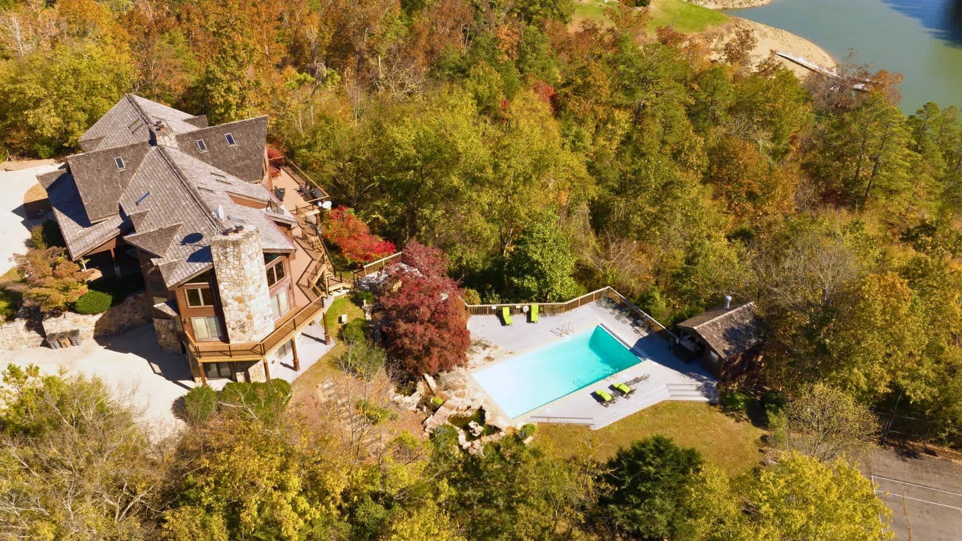 A large house with a swimming pool, surrounded by trees and a lake.