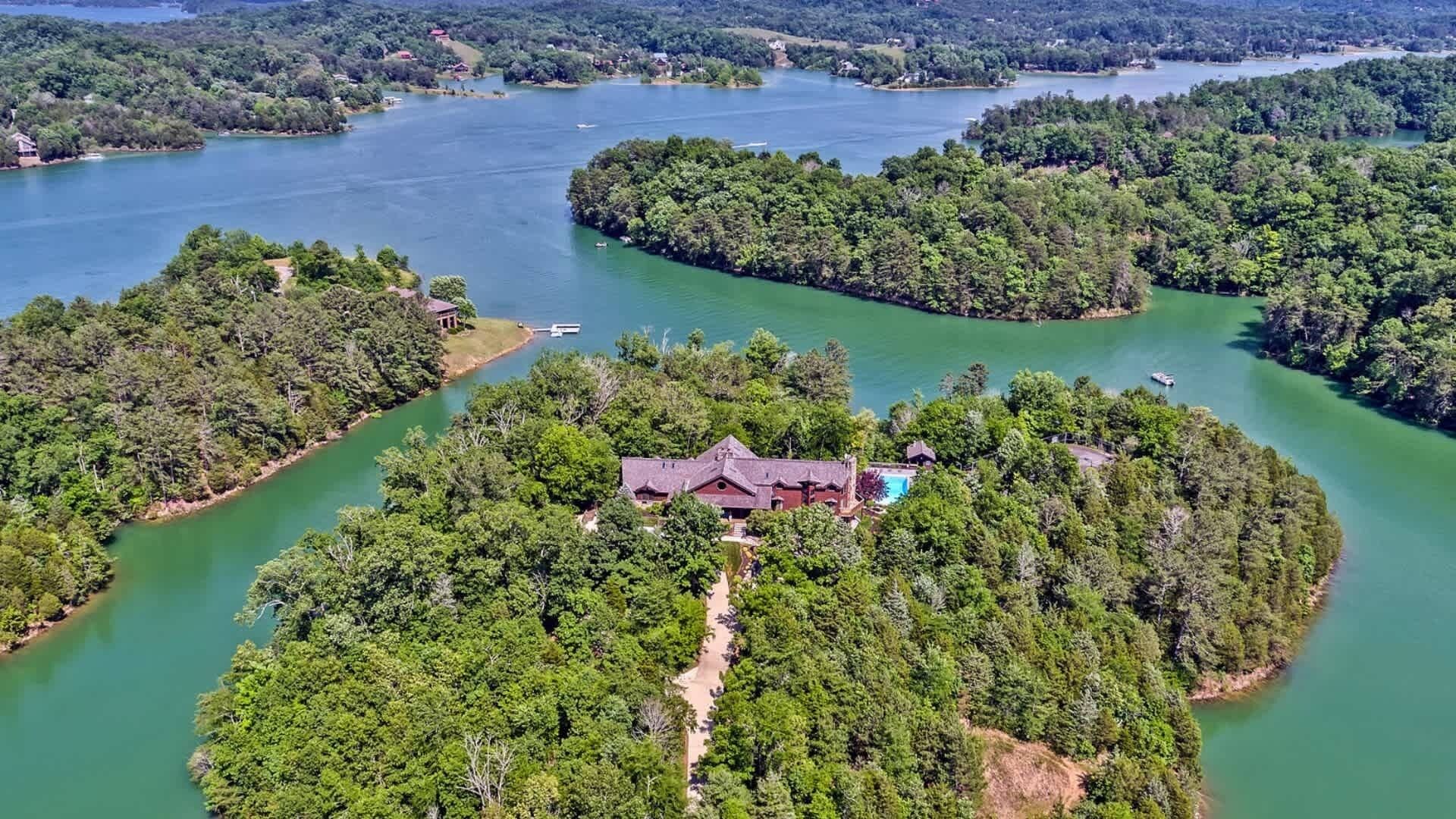 An aerial view of a secluded island with a large house surrounded by dense forest and a lake.
