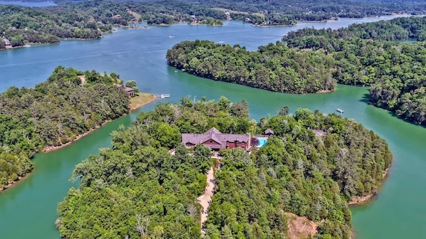 An aerial view of a secluded island with a large house surrounded by dense forest and a lake.