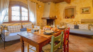 A cozy dining area with a wooden table set for a meal, a fireplace, and a comfortable seating area with cushions.