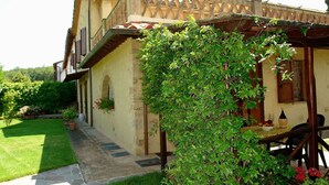 A rustic building with a covered patio, stone steps, and a lush garden.