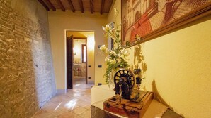 A hallway with a stone wall, a wooden bench, a vintage sewing machine, and a framed tapestry on the wall.