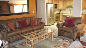 A living room with a brown leather sofa, a glass coffee table, and a patterned rug. - Killington ski house (Stockbridge)