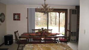 A dining area with a large table, chairs, a chandelier, and a view of the forest through a glass door. - Killington ski house (Stockbridge)