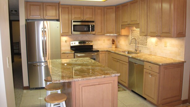 A kitchen with wooden cabinets, stainless steel appliances, a granite countertop, and bar stools. - Killington ski house (Stockbridge)