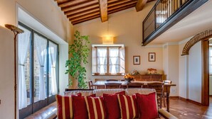 A spacious living room with a wooden ceiling, a large sofa with red cushions, a dining area with a table and chairs, and a staircase leading to an upper level. - Private Villa with WIFI, private pool, TV, balcony, pets allowed, panoramic view, close to Cortona (Castiglion Fiorentino)