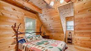 Ein gemütliches Schlafzimmer in einer Blockhütte mit einem Bett, einem Nachttisch und einem kleinen Stuhl.