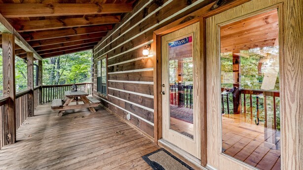 Eine Holzhütte mit überdachter Veranda, einer Holztür und Blick auf den umliegenden Wald.