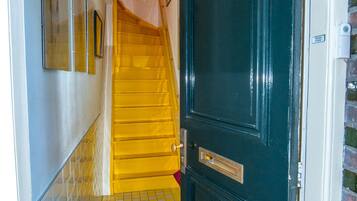 Un couloir doté d’un sol carrelé, d’une porte noire avec une poignée en laiton et d’un escalier aux marches jaunes.