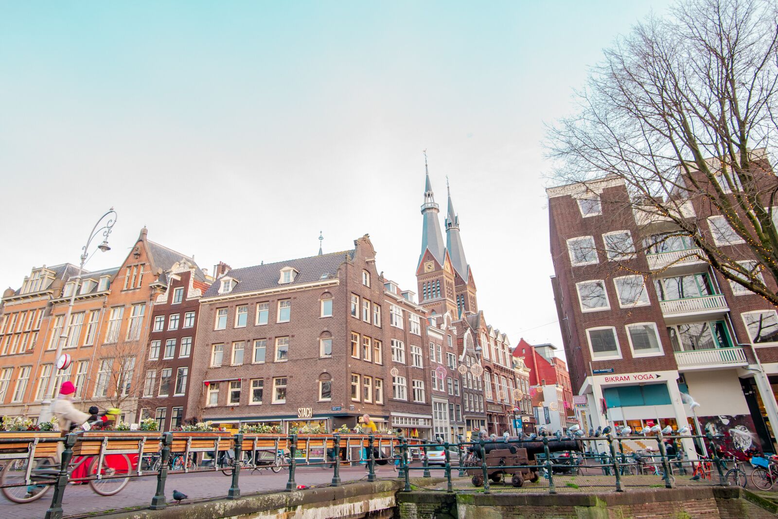 A historic European cityscape with traditional architecture, a prominent church spire, and a canal with a bridge.