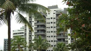 A multi-story residential building with balconies, surrounded by palm trees and greenery. - Excellent 135 m2 apartment 70 m from the sea, with electric barbecue and Wi-Fi  (BERTIOGA)
