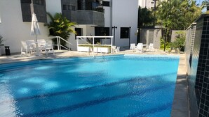 A swimming pool with clear blue water, surrounded by white lounge chairs and a small umbrella. - Excellent 135 m2 apartment 70 m from the sea, with electric barbecue and Wi-Fi  (BERTIOGA)