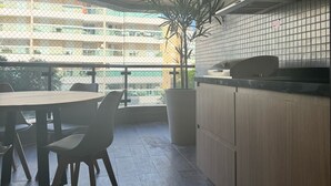 A modern kitchen with wooden cabinets, a large window, and a view of a building across the street. - Excellent 135 m2 apartment 70 m from the sea, with electric barbecue and Wi-Fi  (BERTIOGA)