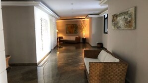 A hallway with a woven sofa, a painting on the wall, and a lamp. - Excellent 135 m2 apartment 70 m from the sea, with electric barbecue and Wi-Fi  (BERTIOGA)