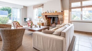Una sala de estar acogedora con chimenea, un sofá, una mesa de comedor y una silla de mimbre.