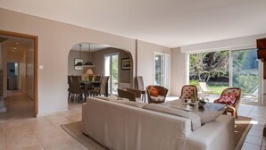 Un salón amplio con un sofá grande, comedor con sillas y vistas al exterior mediante puertas correderas.