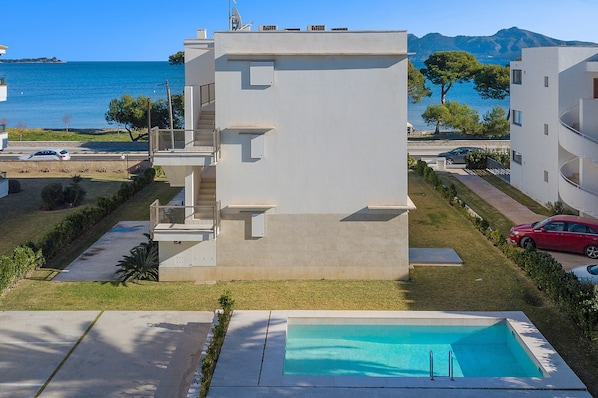 A modern building with a pool, located near a body of water and mountains.