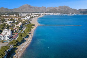 An aerial view of a coastal town with a beach, buildings, and mountains in the background.
