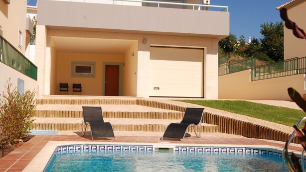 Un edificio di due piani con piscina, due sdraio e una veranda coperta.