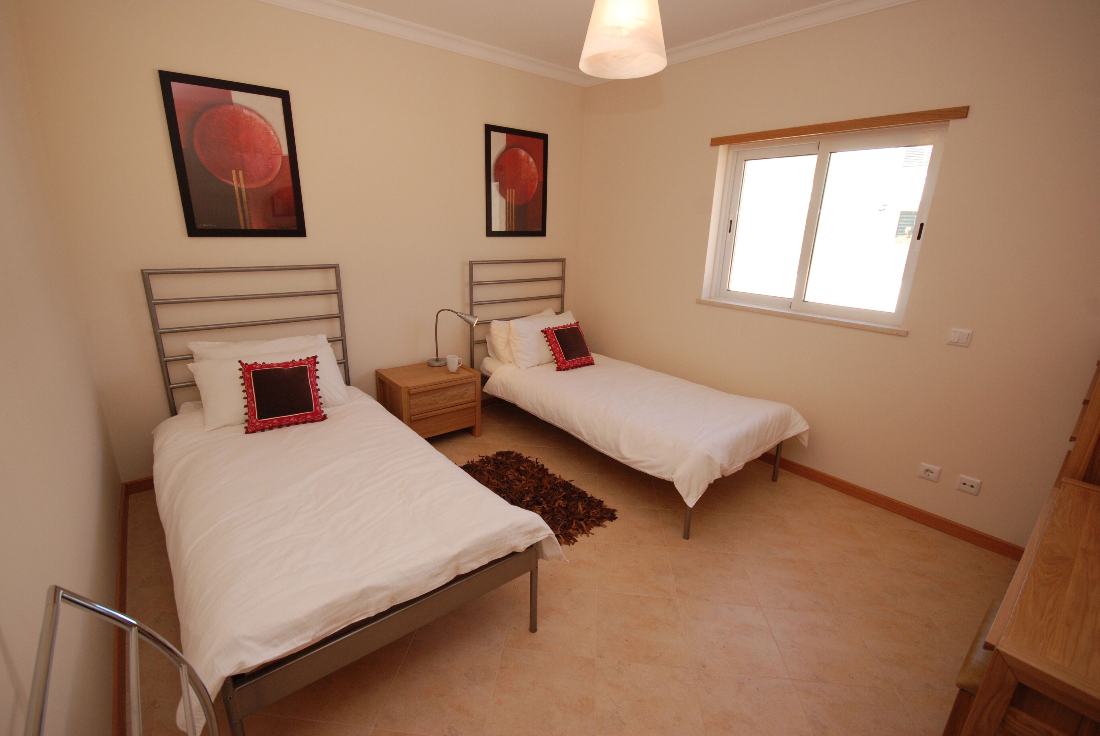 A bedroom with two beds, a window, and artwork on the walls.