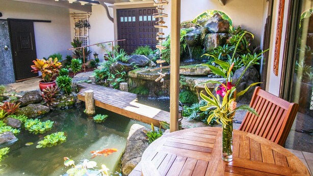 Un jardin paisible avec un bassin à carpes koï, un pont en bois et une table sur laquelle est posé un vase.