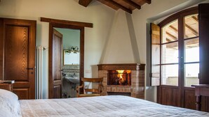 Un dormitori amb un llit gran, una llar de foc, bigues de fusta i vistes per la finestra.