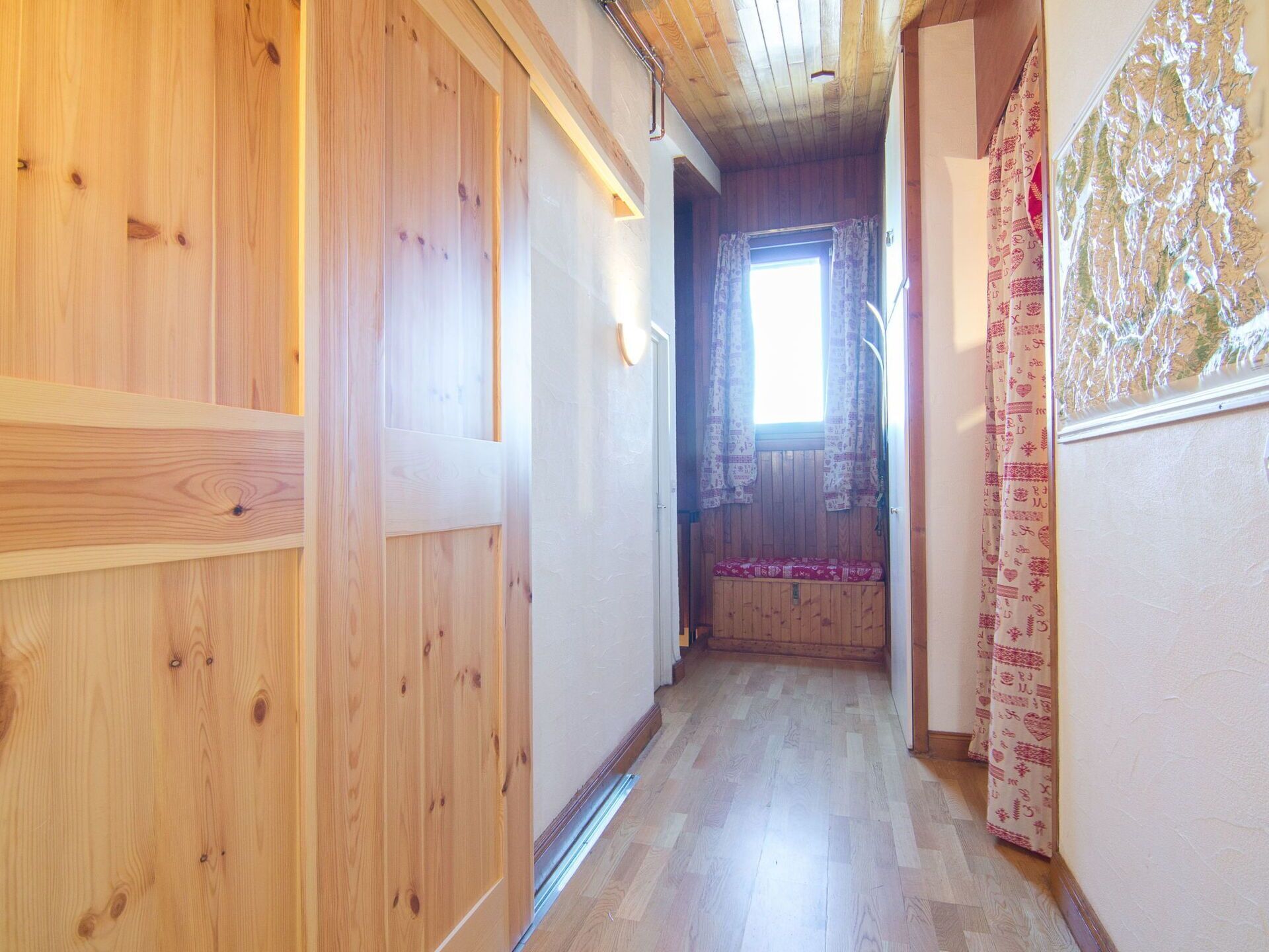 Ein Holzflur mit einer Bank, einem Fenster mit Vorhängen und einer Wand mit Muster.