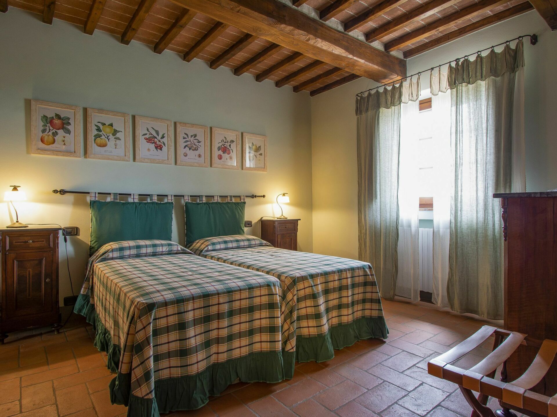 Une chambre avec deux lits, un plafond en bois, une fenêtre avec des rideaux et des reproductions encadrées de motifs botaniques au mur.