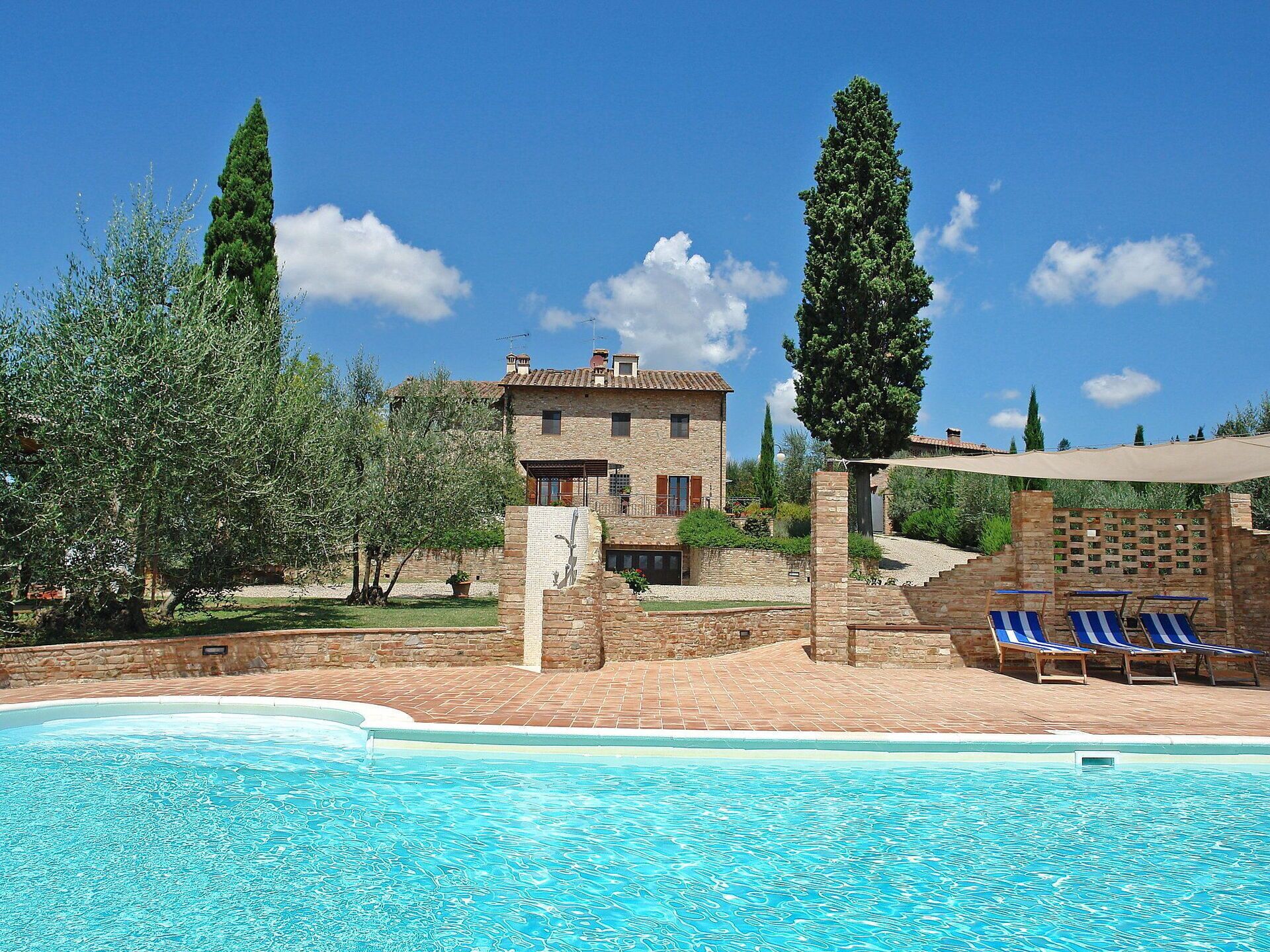 A poolside area with a stone building, a pergola, and lounge chairs.