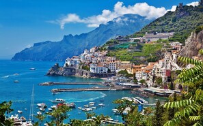 A coastal town with buildings on a hillside, a harbor with boats, and a castle on a cliff. - between Amalfi, Pompei, Paestum, Positano (Salerno)