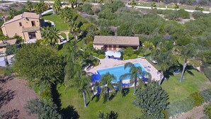 Vista aérea de uma propriedade com piscina, vários edifícios e vegetação exuberante.