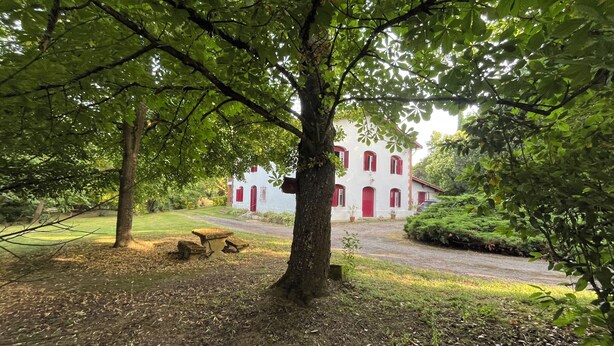 A white building with red doors and windows, surrounded by trees and a gravel path. - Mansion of an old farm, cottage in France, quiet and romantic stay in the Gers (Gavarret-Sur-Aulouste)