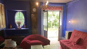 A room with a red sofa, a wooden table, a clock, and a window with a view of greenery. - Mansion of an old farm, cottage in France, quiet and romantic stay in the Gers (Gavarret-Sur-Aulouste)