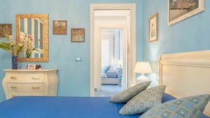 A bedroom with a blue bedspread, a white dresser with a vase of flowers, and a door leading to another room. - Wonderful private villa for 6 people with WIFI, A/C, private pool, TV and patio (Cefalù)