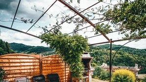 Un patio al aire libre con mesa y sillas, rodeado por una valla de madera y vistas a un paisaje montañoso.
