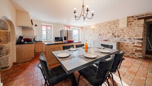 Una cocina con pared de piedra, una mesa de comedor dispuesta con platos y vasos, y una araña.