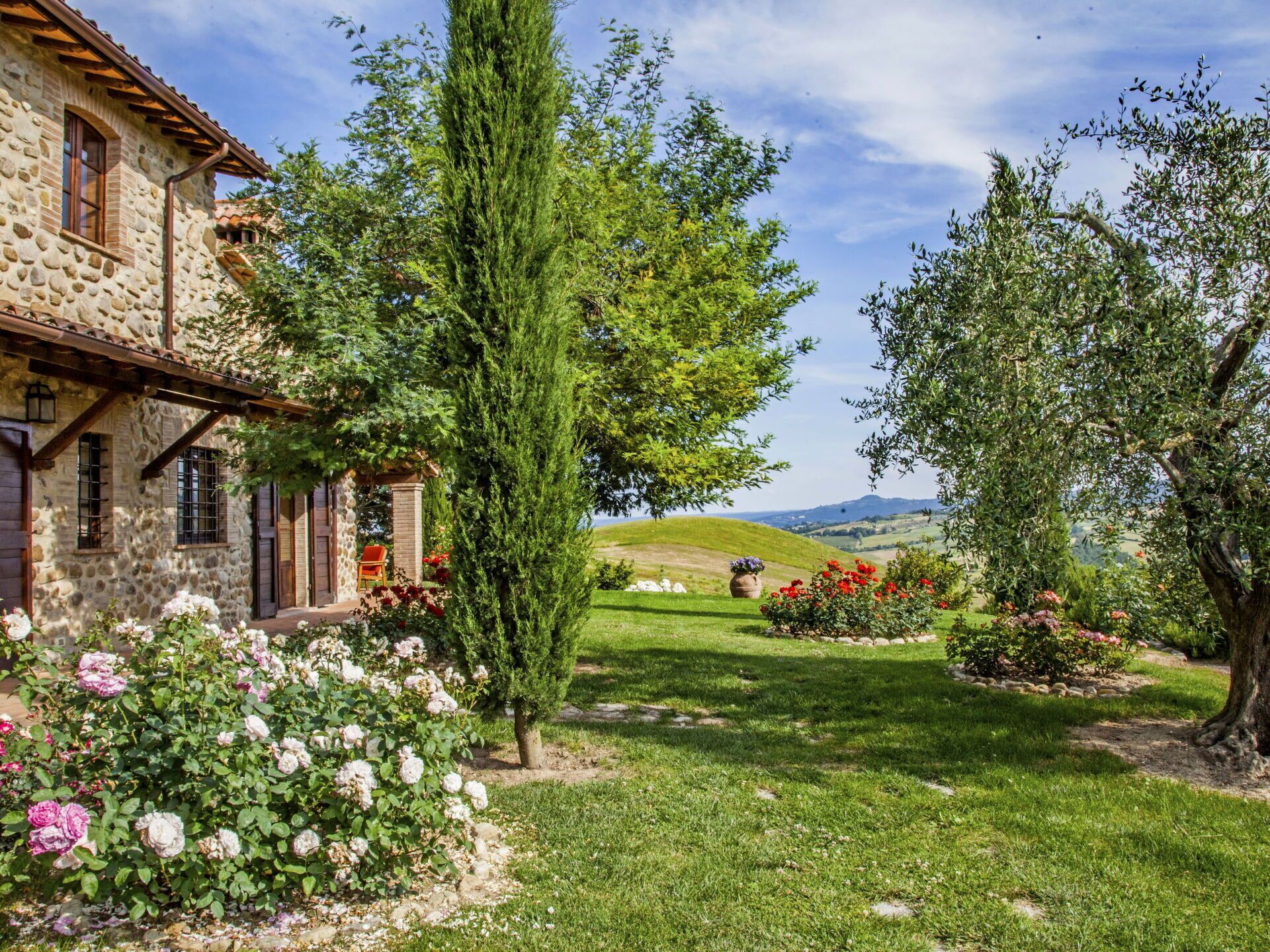 A stone house with a garden, a tall tree, and a view of rolling hills.