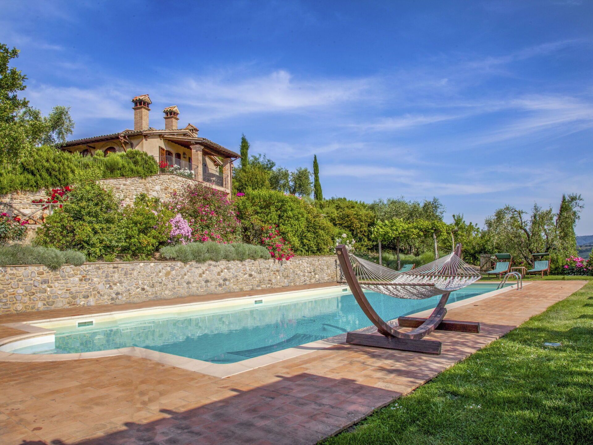 A pool area with a hammock, stone walls, and a house in the background.
