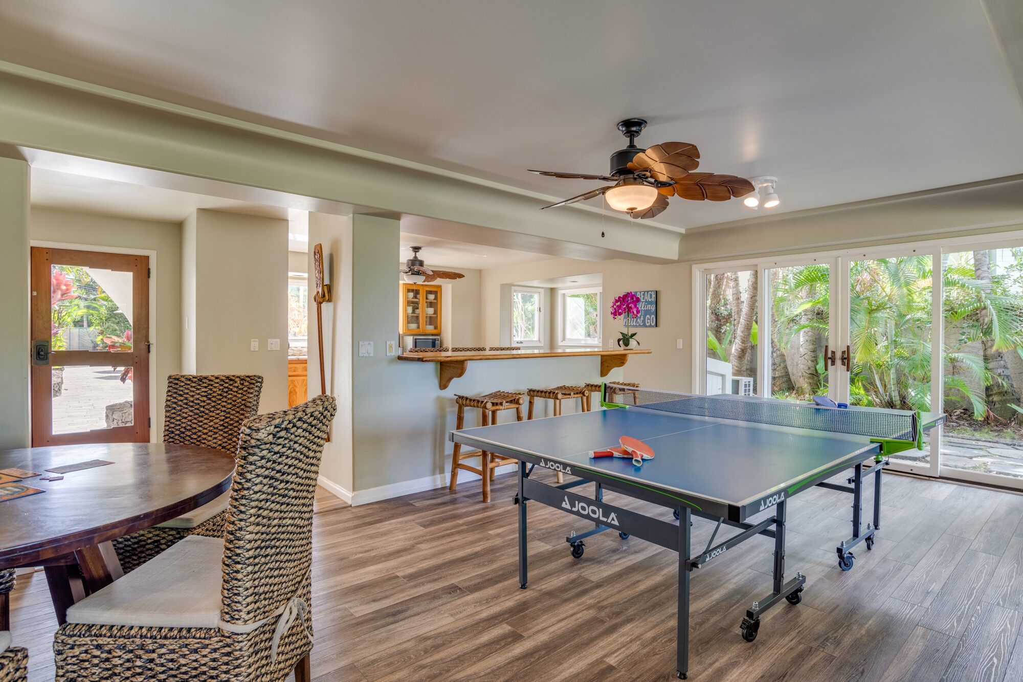 Une pièce spacieuse équipée d’une table de ping-pong, de sièges confortables, d’un coin cuisine et de grandes fenêtres donnant sur un paysage verdoyant.