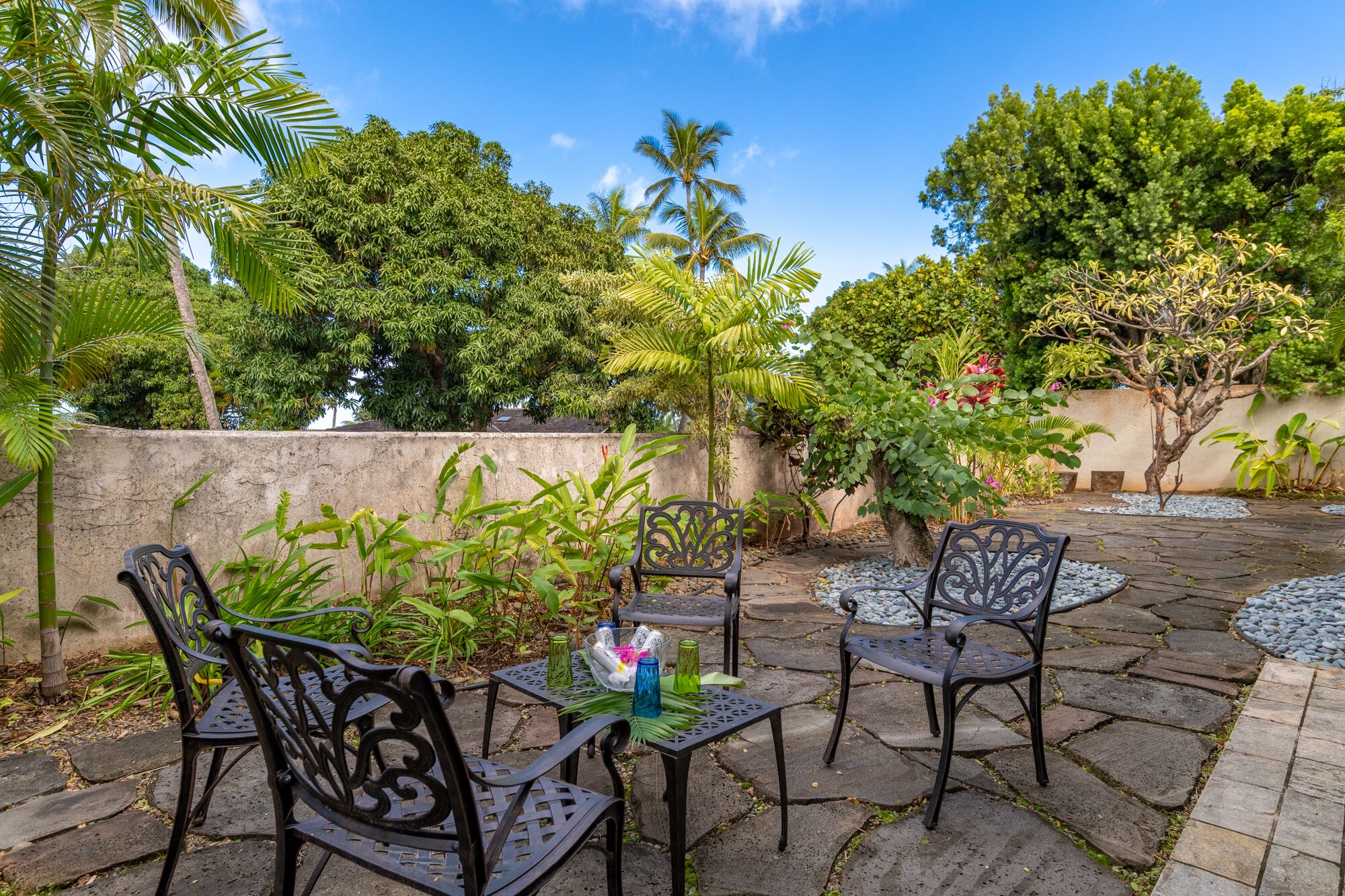 An outdoor patio with stone flooring, metal chairs, and a small table with decorative items.