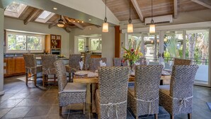 A spacious dining area with high ceilings and exposed beams, featuring a large table and multiple chairs with patterned upholstery.