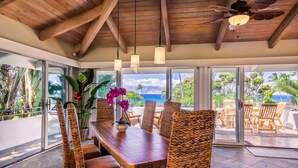 A dining area with wicker chairs, a wooden table, and a view of the ocean.