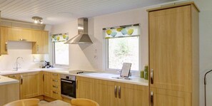 Une cuisine moderne avec des meubles en bois, une hotte de cuisinière en acier inoxydable et une fenêtre agrémentée de rideaux décoratifs.