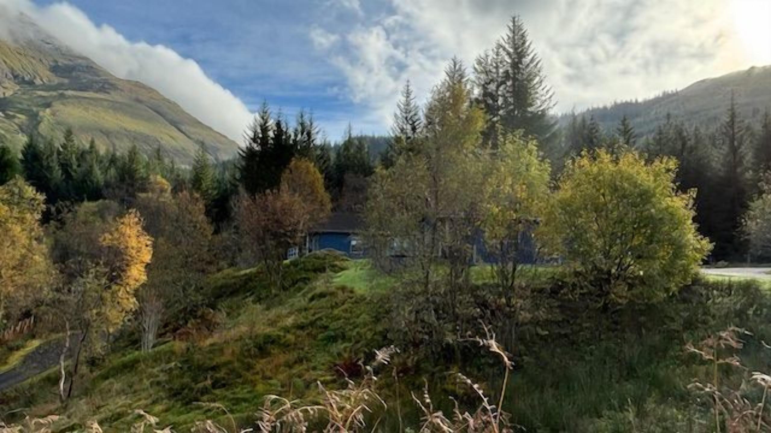 Paisagem montanhosa com uma casa rodeada por árvores e vegetação.