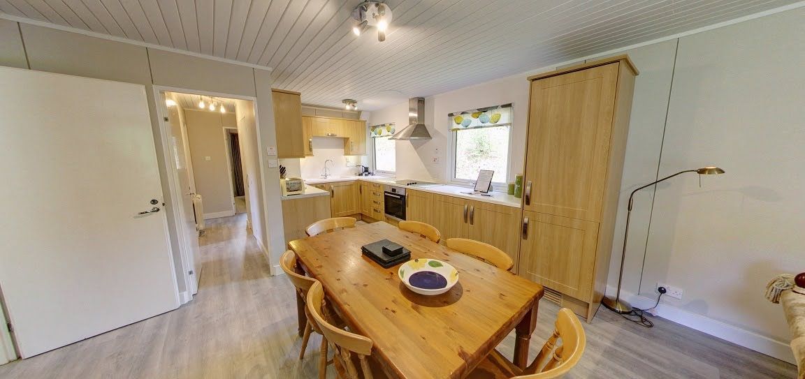 A compact kitchen with wooden cabinets, a dining table with chairs, and a small island with a bowl.