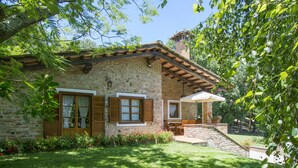 A stone house with wooden shutters, a covered patio, and a garden.