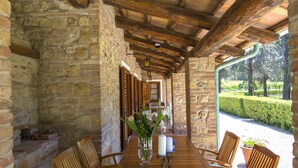 A stone-walled room with wooden beams, a wooden table with chairs, and a view of a garden.