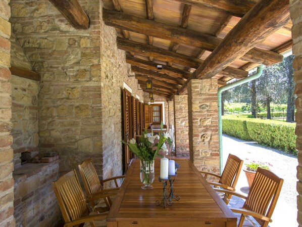 A stone-walled room with wooden beams, a wooden table with chairs, and a view of a garden.