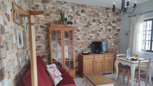Ein Wohnzimmer mit rotem Sofa, Holzschrank, Fernseher und einem Essbereich mit Tisch und Stühlen.