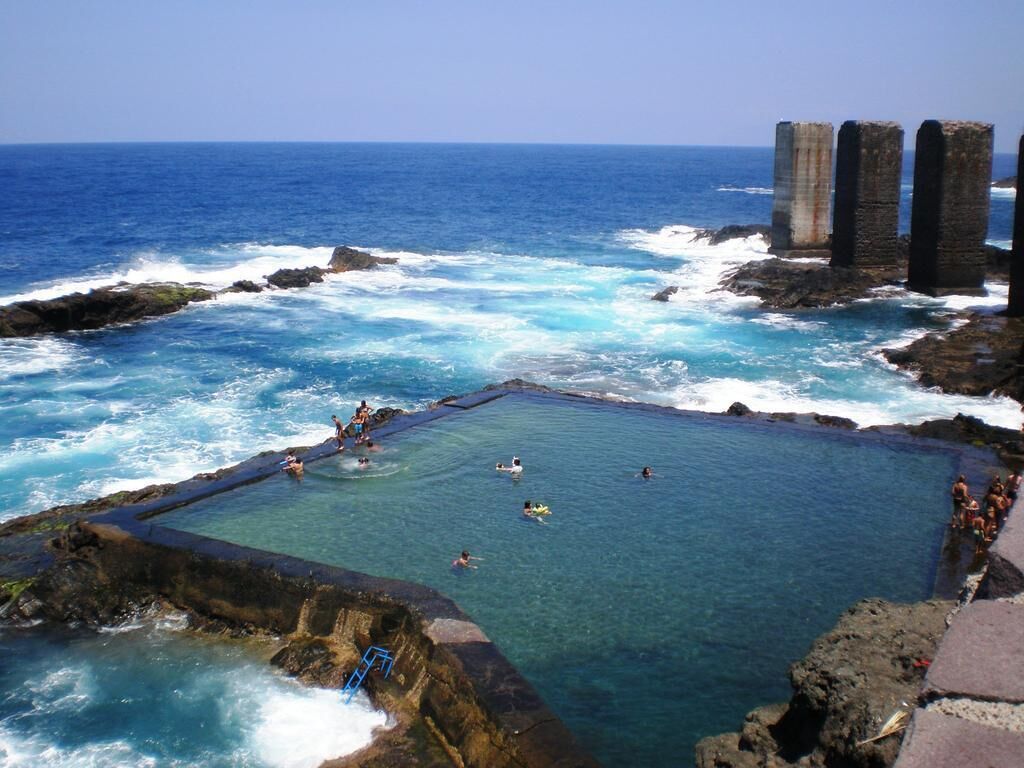 A coastal swimming area with clear water, rocky formations, and a view of the ocean.